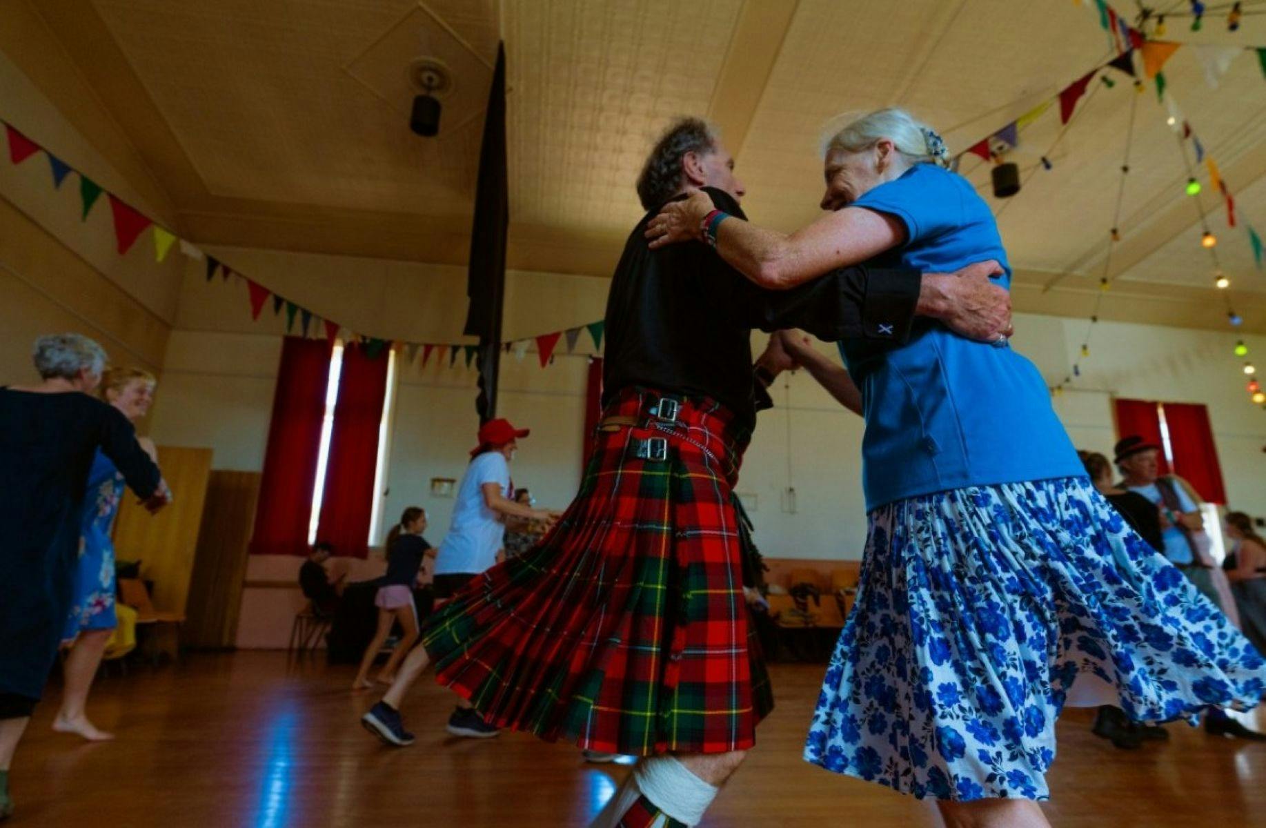 Couple dancing.  Man is in a kilt and woman dressed in blue arm in arm