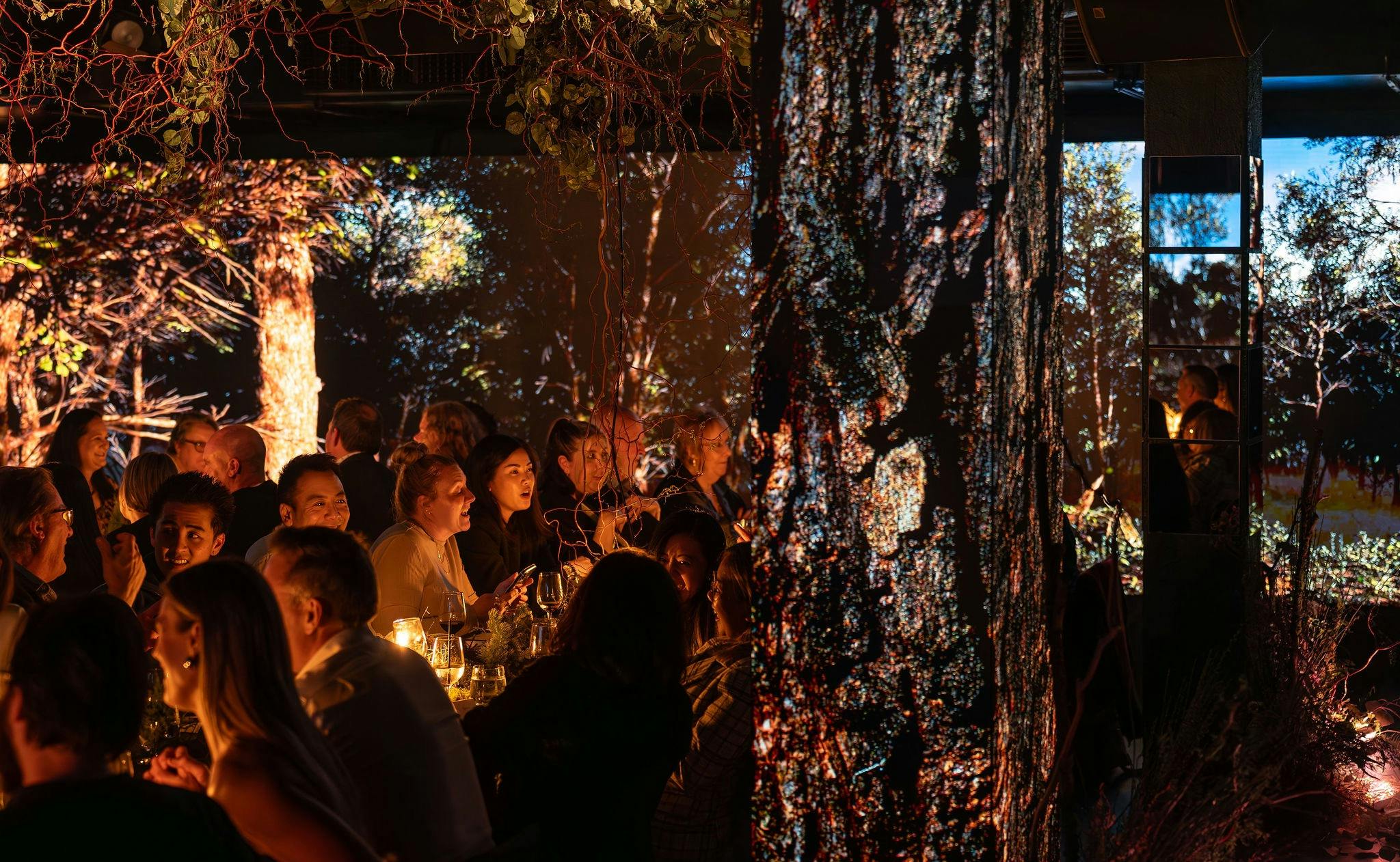 A communal dining table with forest styling and forest displayed on LED screens