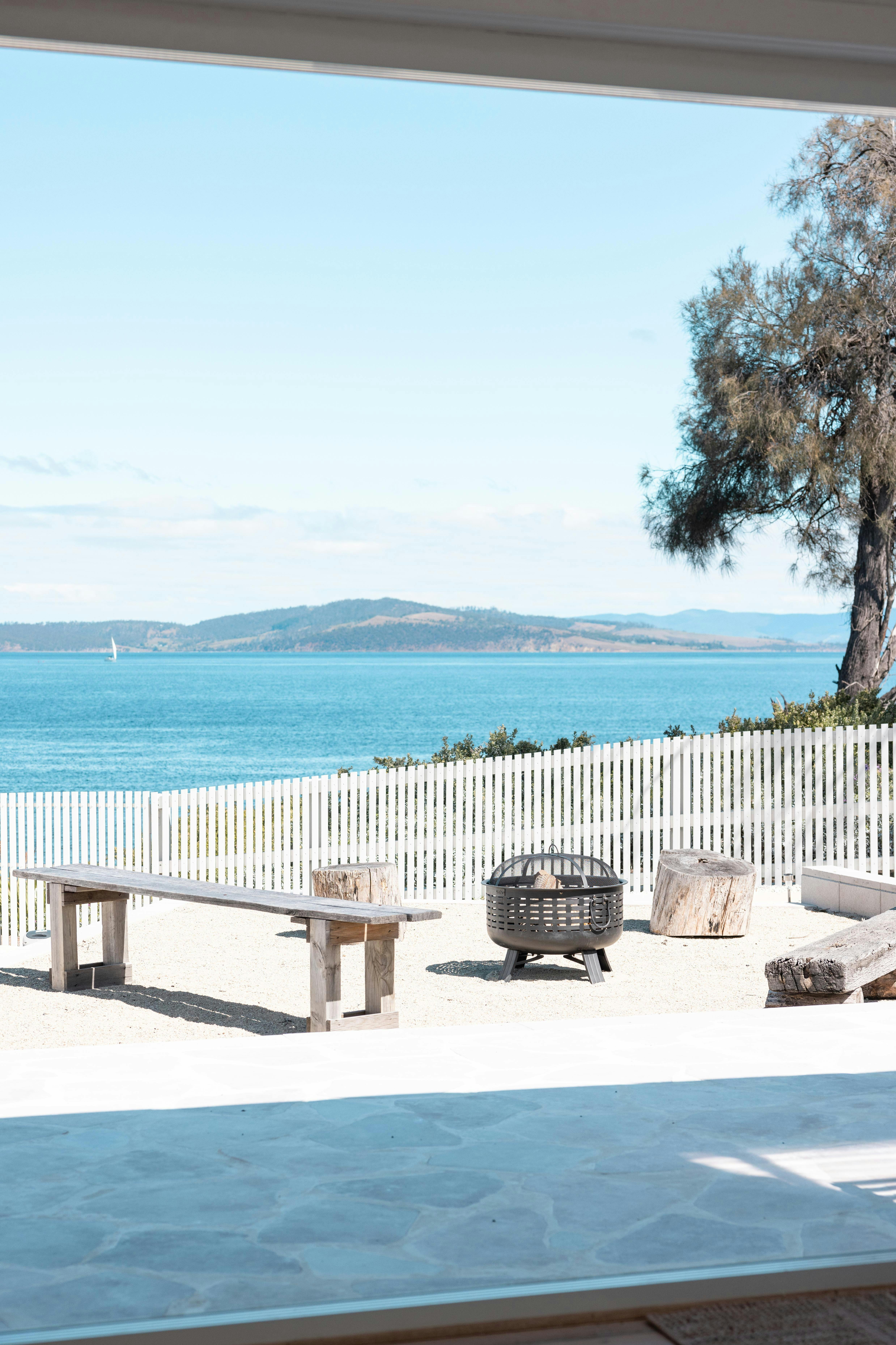 Outdoor fire pit area with wooden benches overlooking a calm ocean view