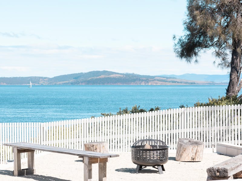 Outdoor fire pit area with wooden benches overlooking a calm ocean view