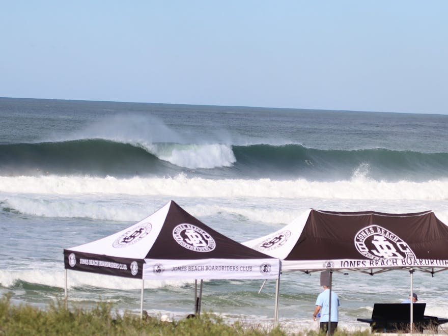 Big waves breaking in oceacn with a jones beach boardriders gazebo up on the beach in foreground