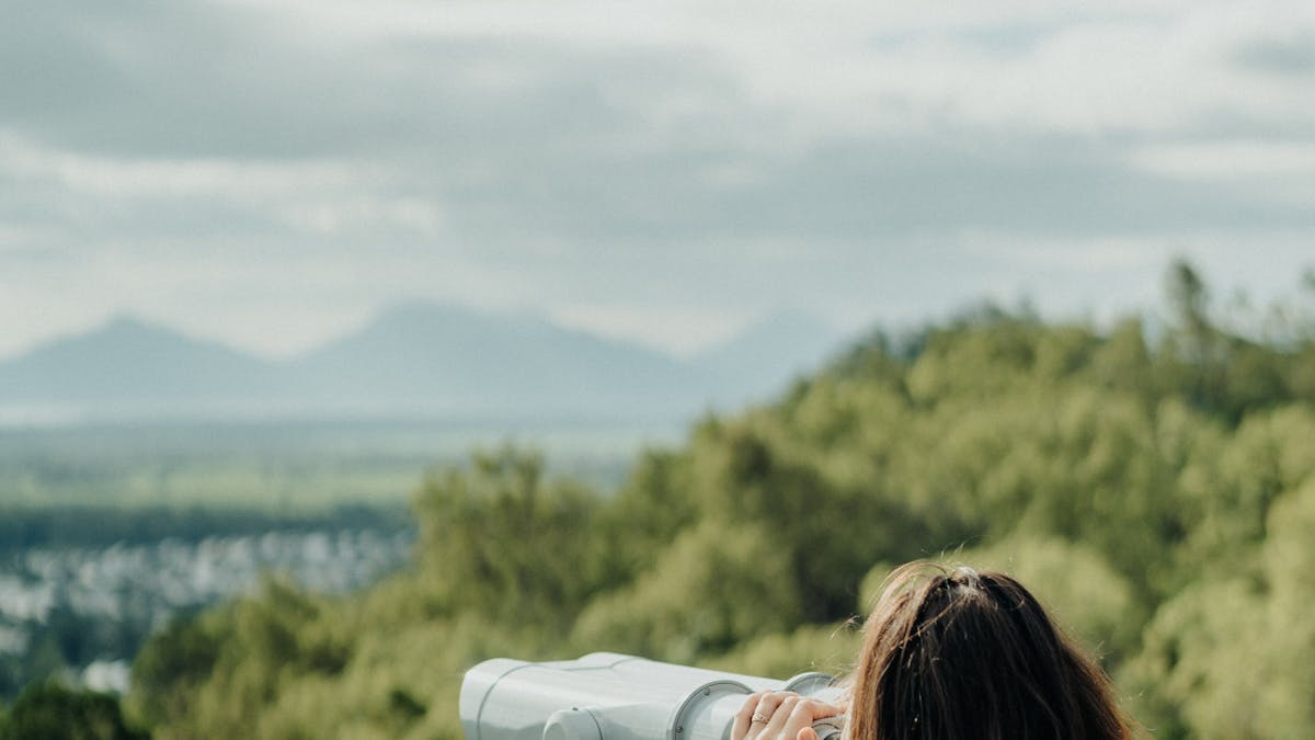 Girl looks through binoculars to rainforest and mountain view