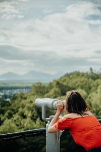 Girl looks through binoculars to rainforest and mountain view