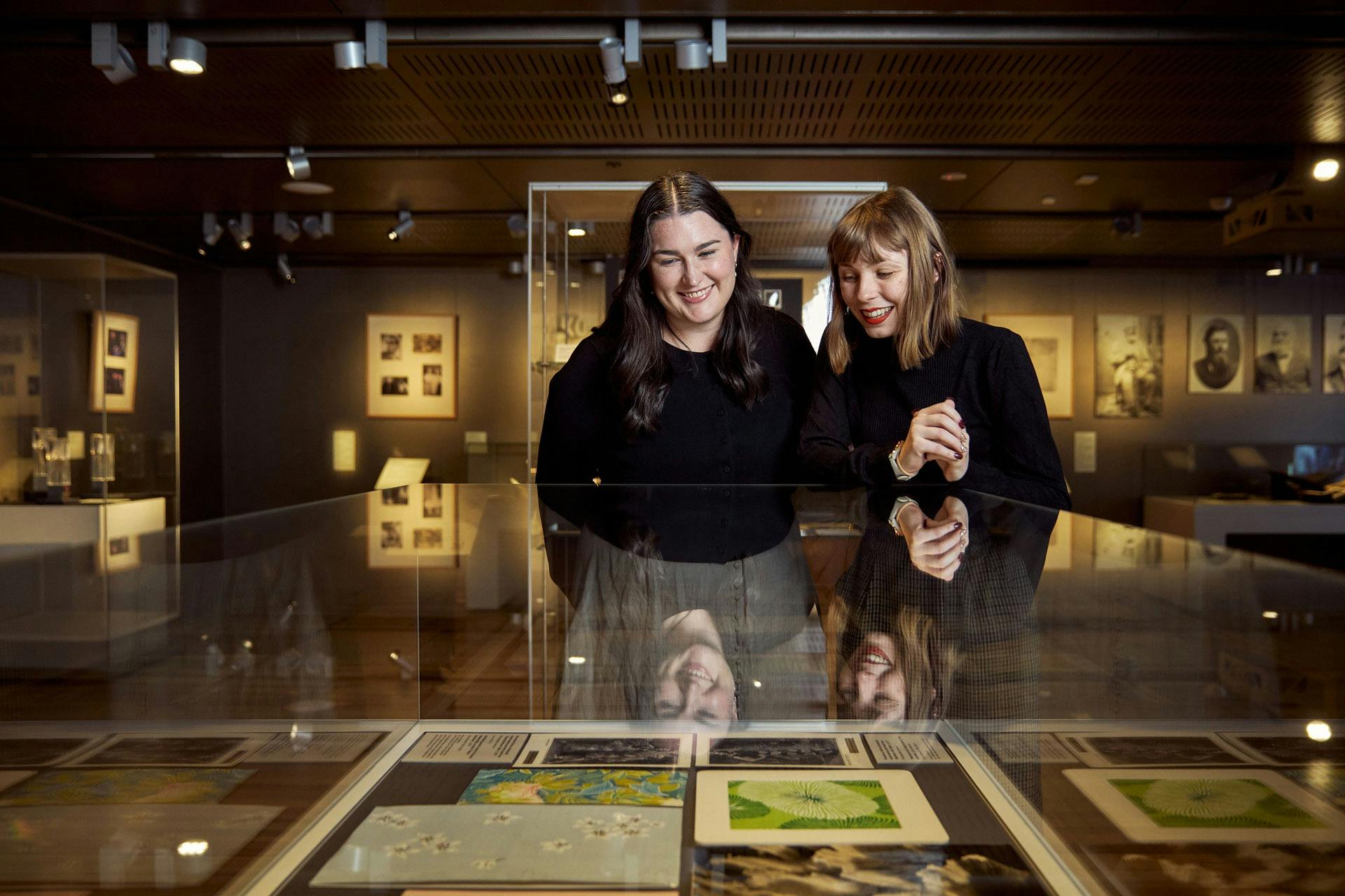 Two women in black looking at documents in display case in low-lighting gallery.