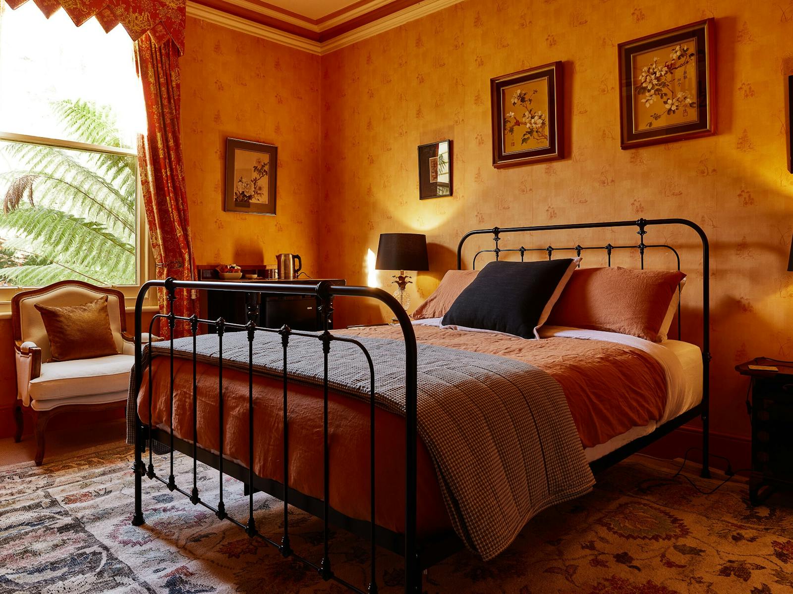 A wrought iron bed sits in a room with yellow wallpaper and heavy red curtains.