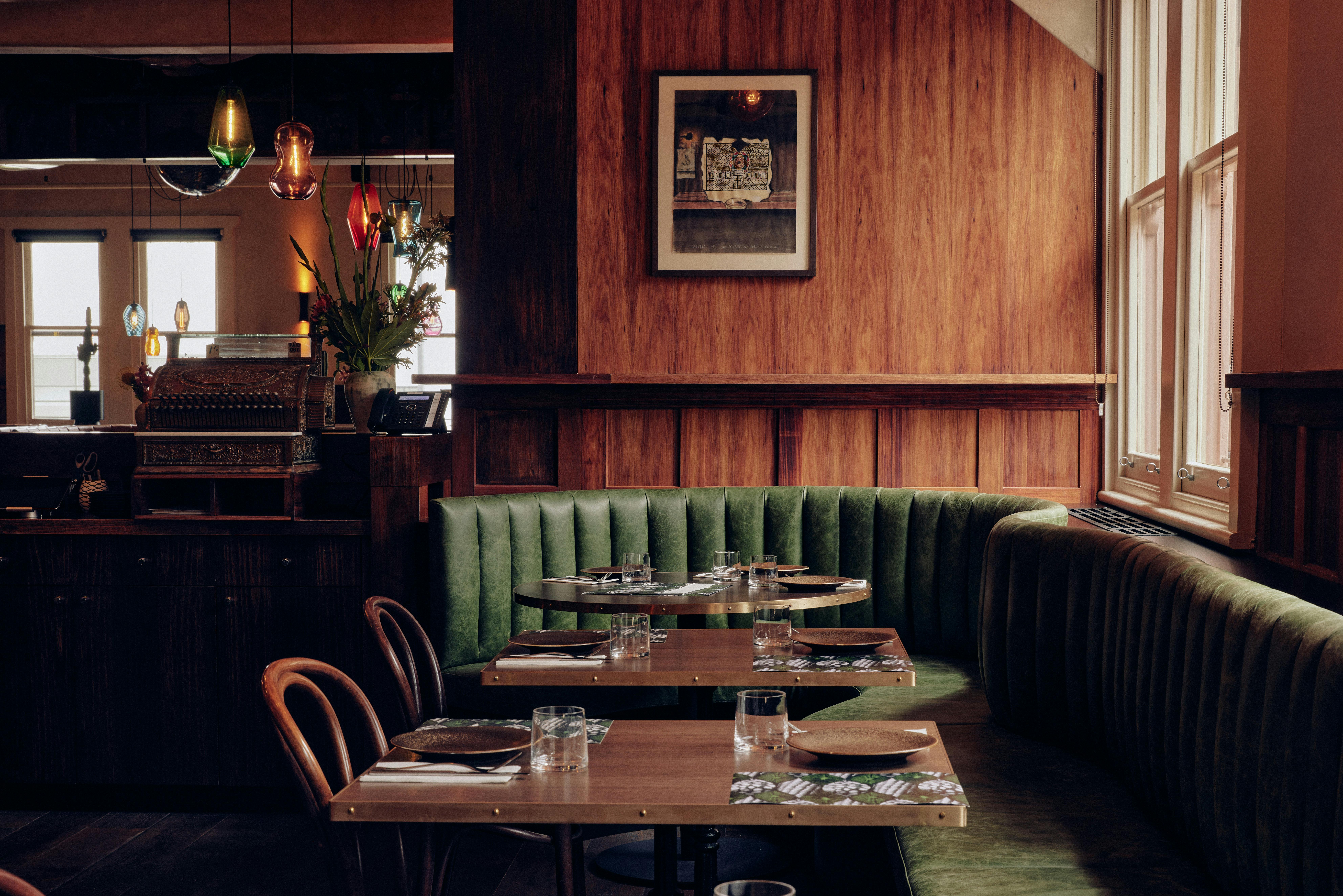 Three tables set with plates and cutlery. Green leather booths, flowers and an artwork in the back.