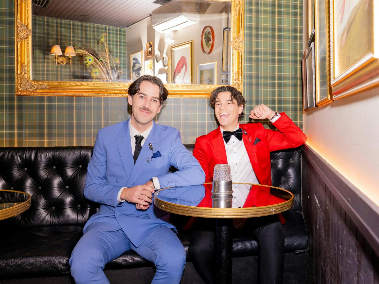 Two men dressed in coloured suits, sitting in booth Two men dressed in coloured suits, sitting in booth
