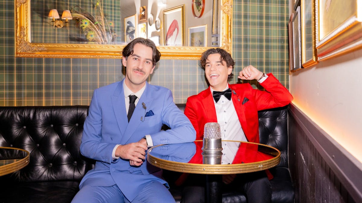 Two men dressed in coloured suits, sitting in booth