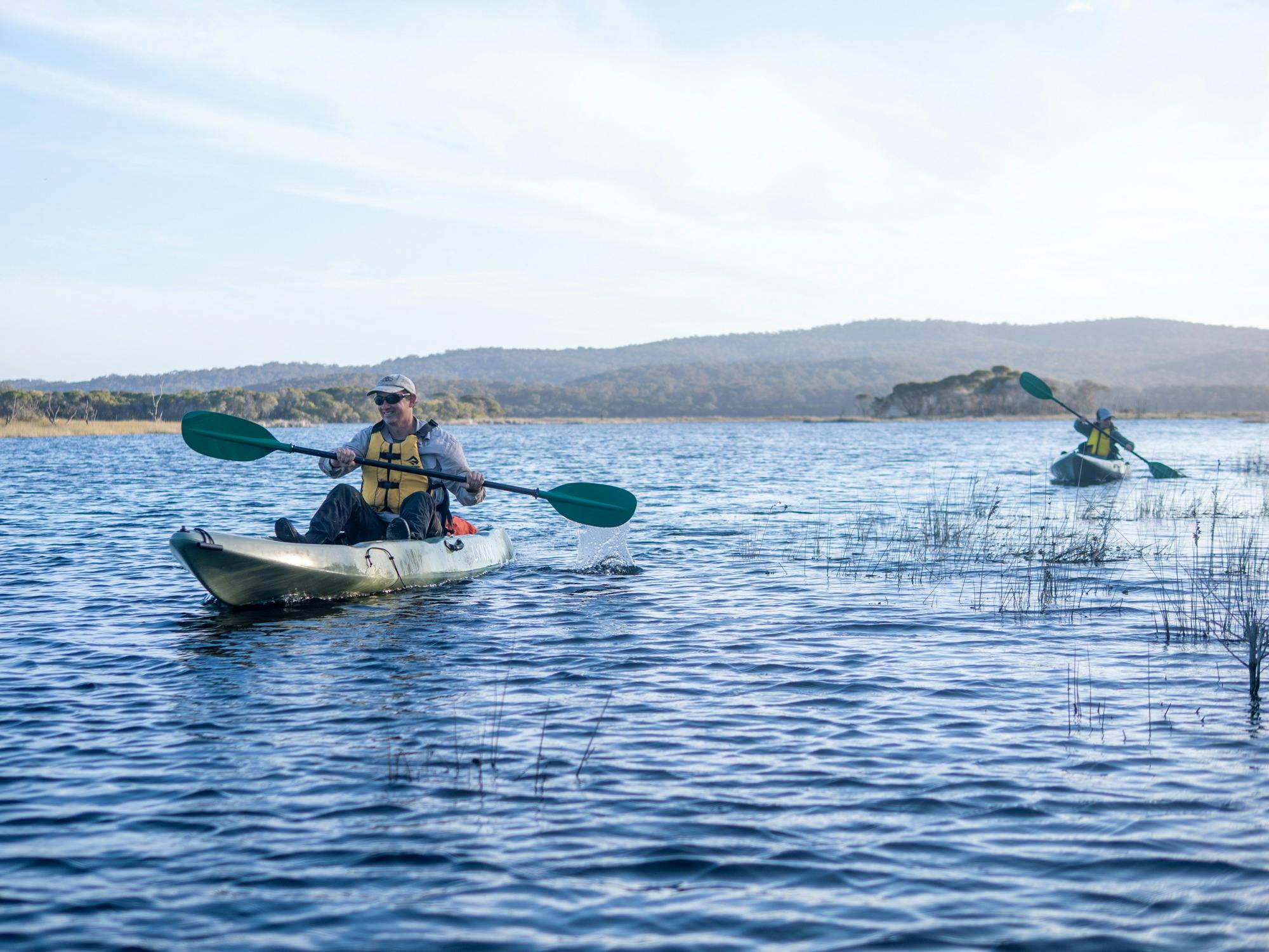 Two kayakers on Wallagoot Lake, illuminated by the warm, low afternoon sun.