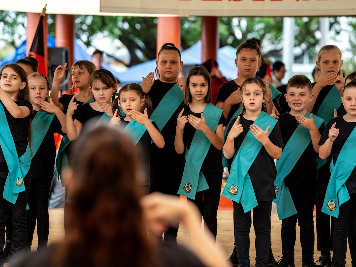 Children in black clothing with blue sashes perform using Auslan at the Mareeba Multicultural Fest.