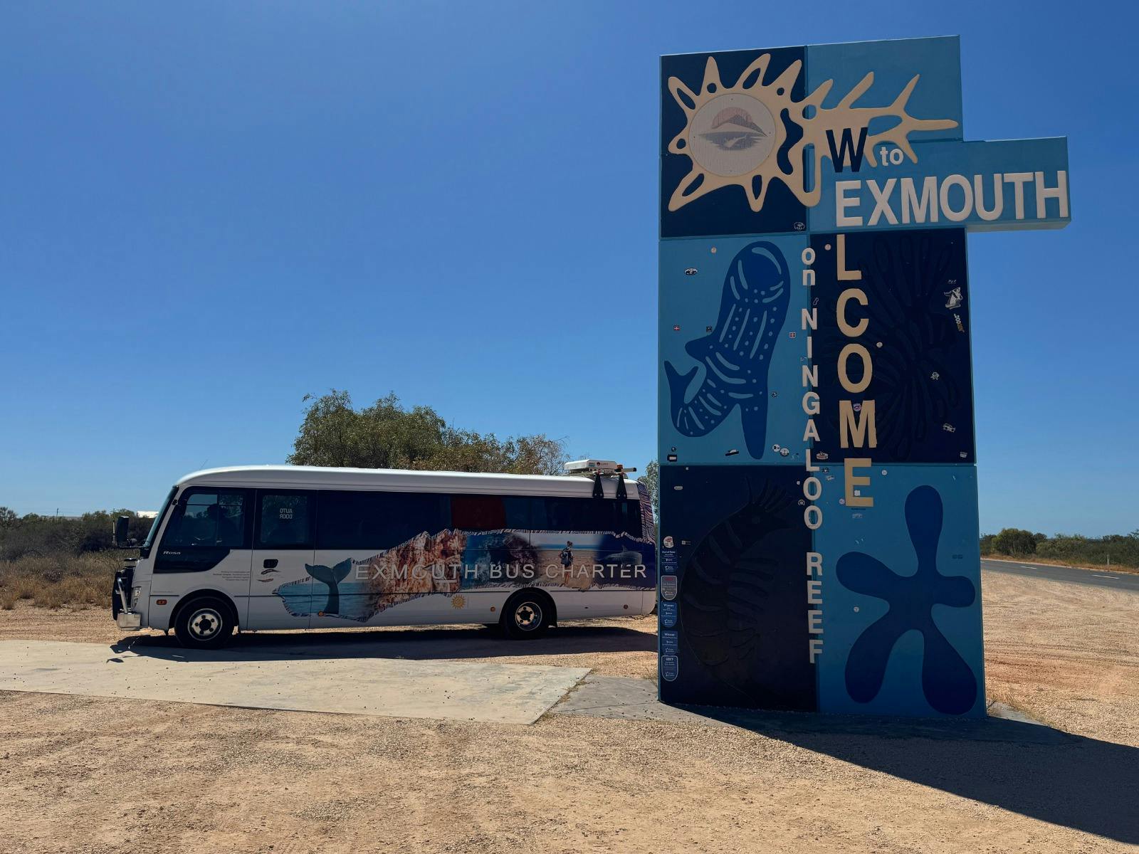 Exmouth Bus Charter vehicle parked beside the Exmouth town entrance sign.