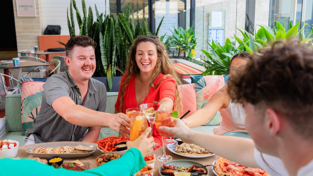 Group of friends cheering and enjoining meals at Hibiscus Bar & Terrace in Hyatt Regency Brisbane