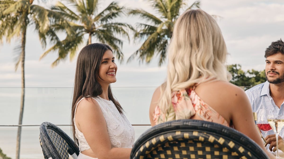 People sitting at table with palm trees in background
