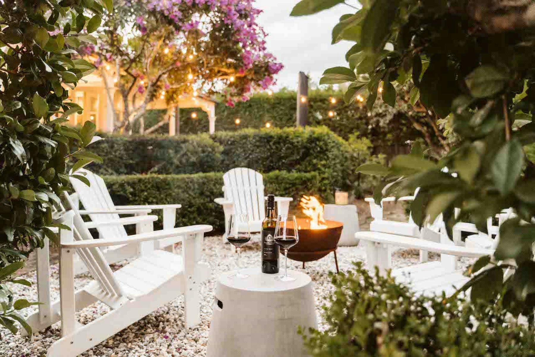 Image - Firepit in the garden lit with a bottle of wine ready to be enjoyed. Gardens surround pit