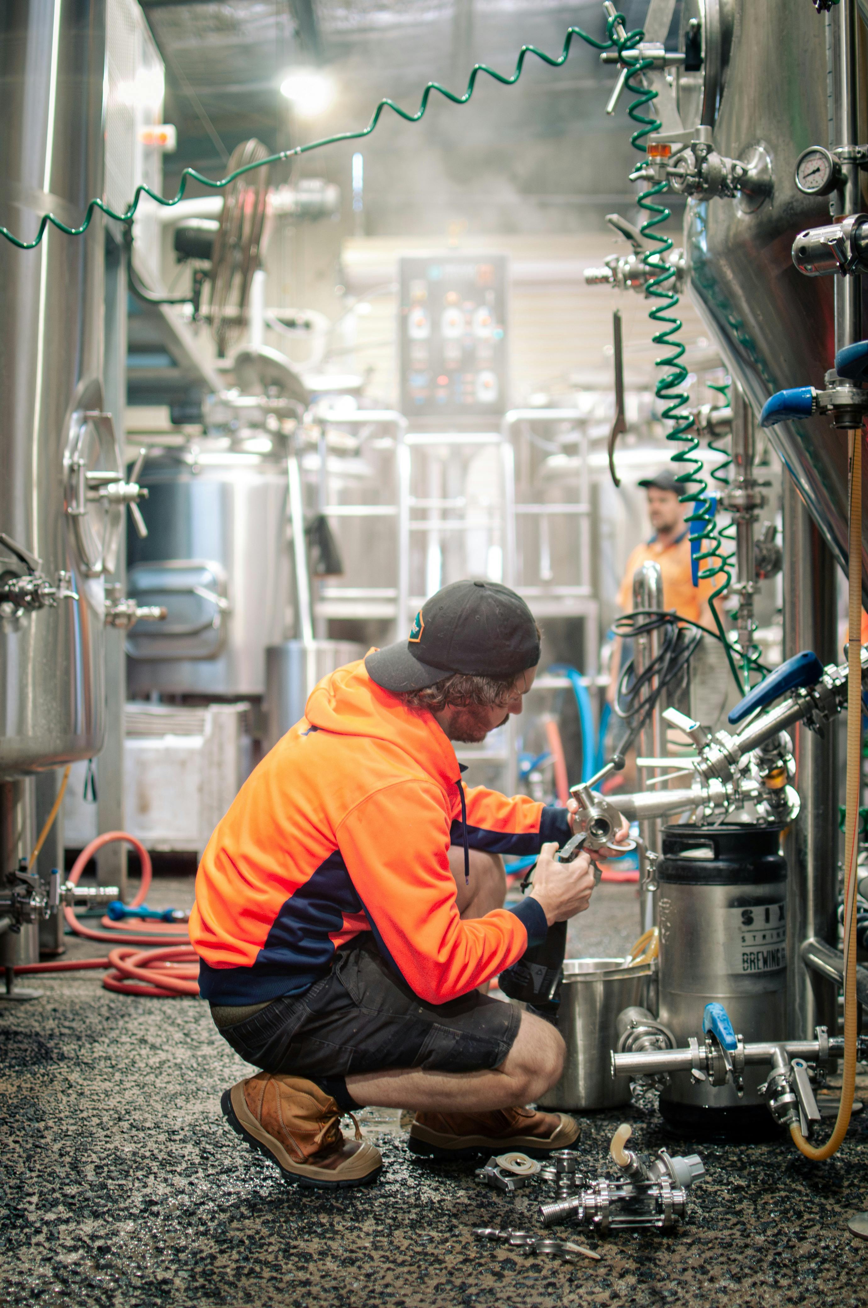 A brewer bent down checking and cleaning tank taps.