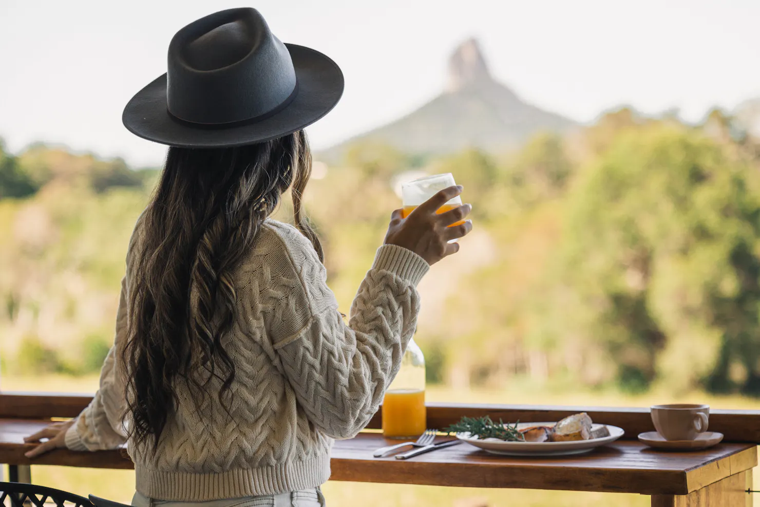 Lady holding drink admiring mountain view while eating breakfast on the balcony of the cabin