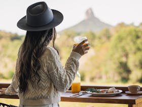 Lady holding drink admiring mountain view while eating breakfast on the balcony of the cabin