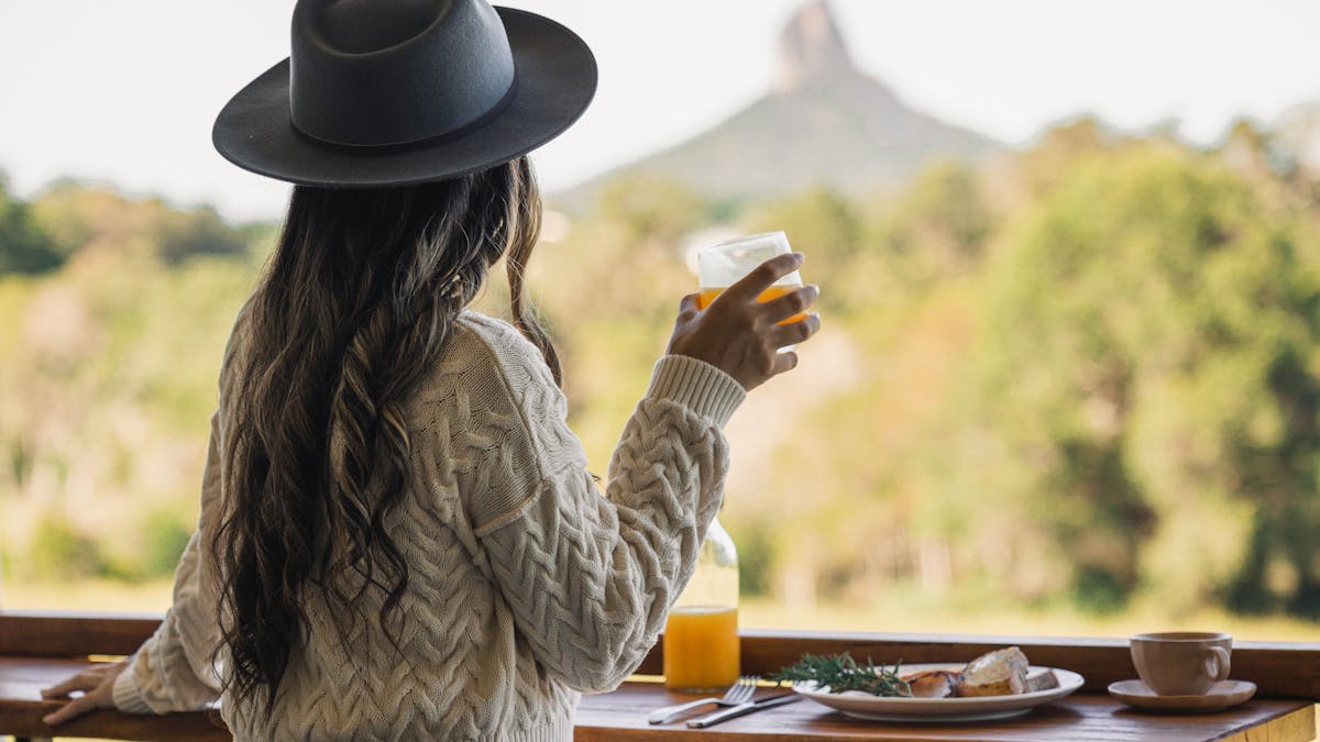 Lady holding drink admiring mountain view while eating breakfast on the balcony of the cabin
