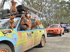 A Bash Car that is Scooby Doo themed with Scooby Doo costume waving out the window.