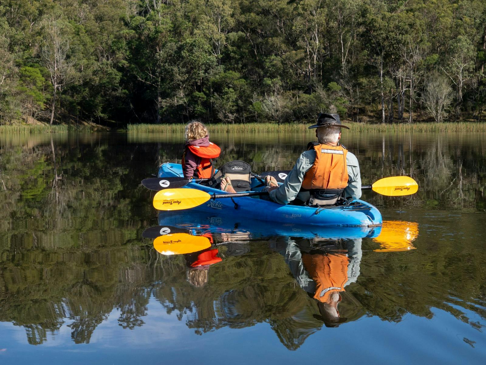 Grandfather and granddaughter resting in kayak on Brogo Dam, enjoying view of Wadbilliga National Pa