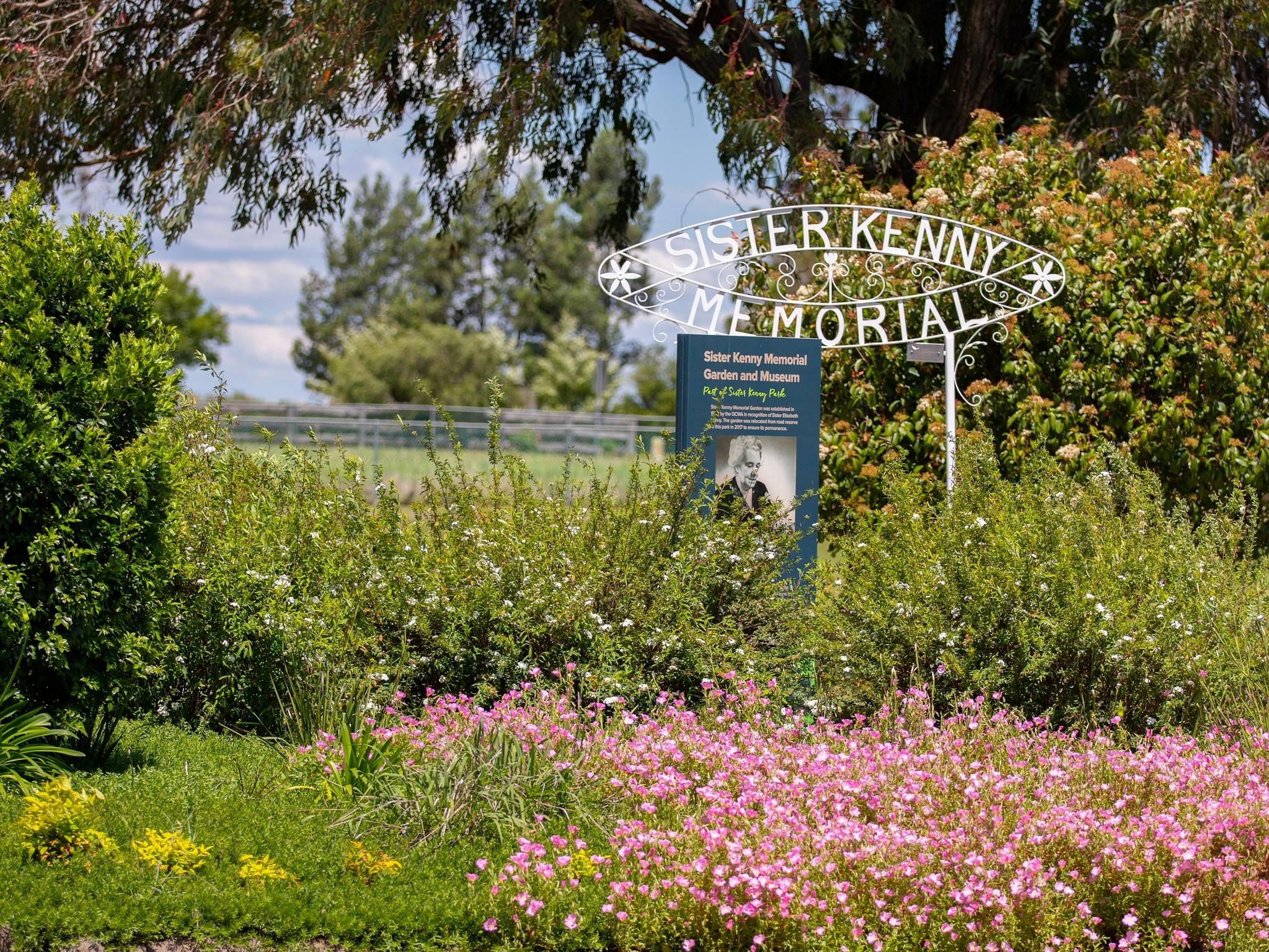 A lush garden with flowers and a sign stating Sister Kenny Memorial. A lush garden with flowers and a sign stating Sister Kenny Memorial.