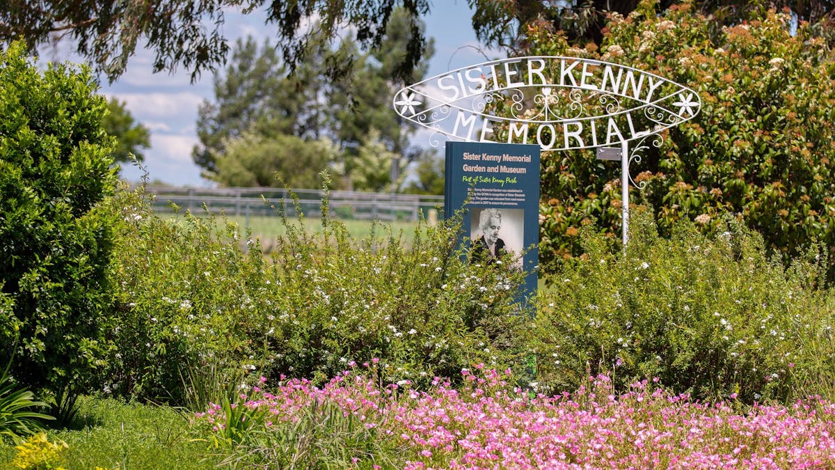 A lush garden with flowers and a sign stating Sister Kenny Memorial.