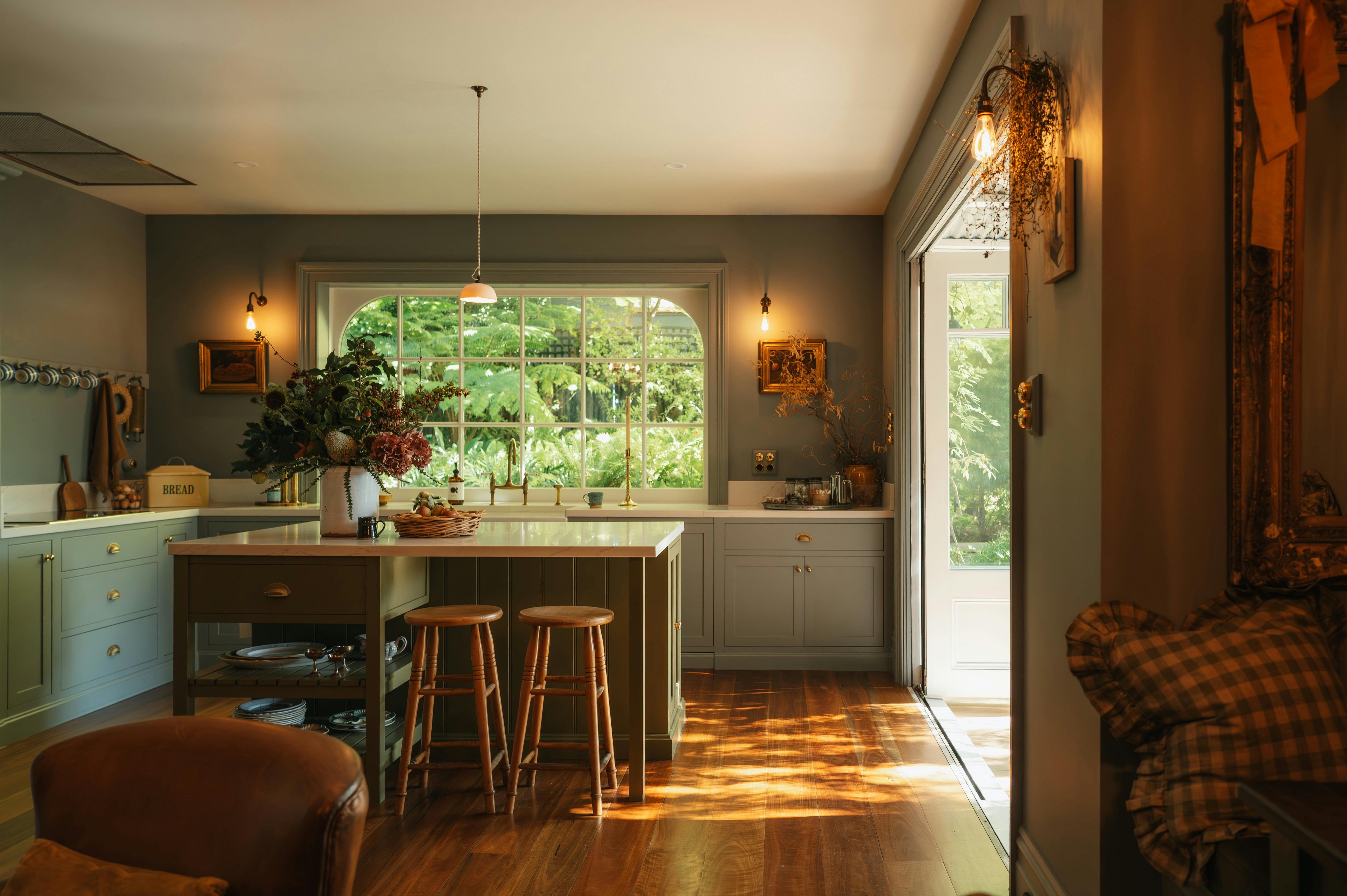 Kitchen with island, stools, large window and garden light beyond.