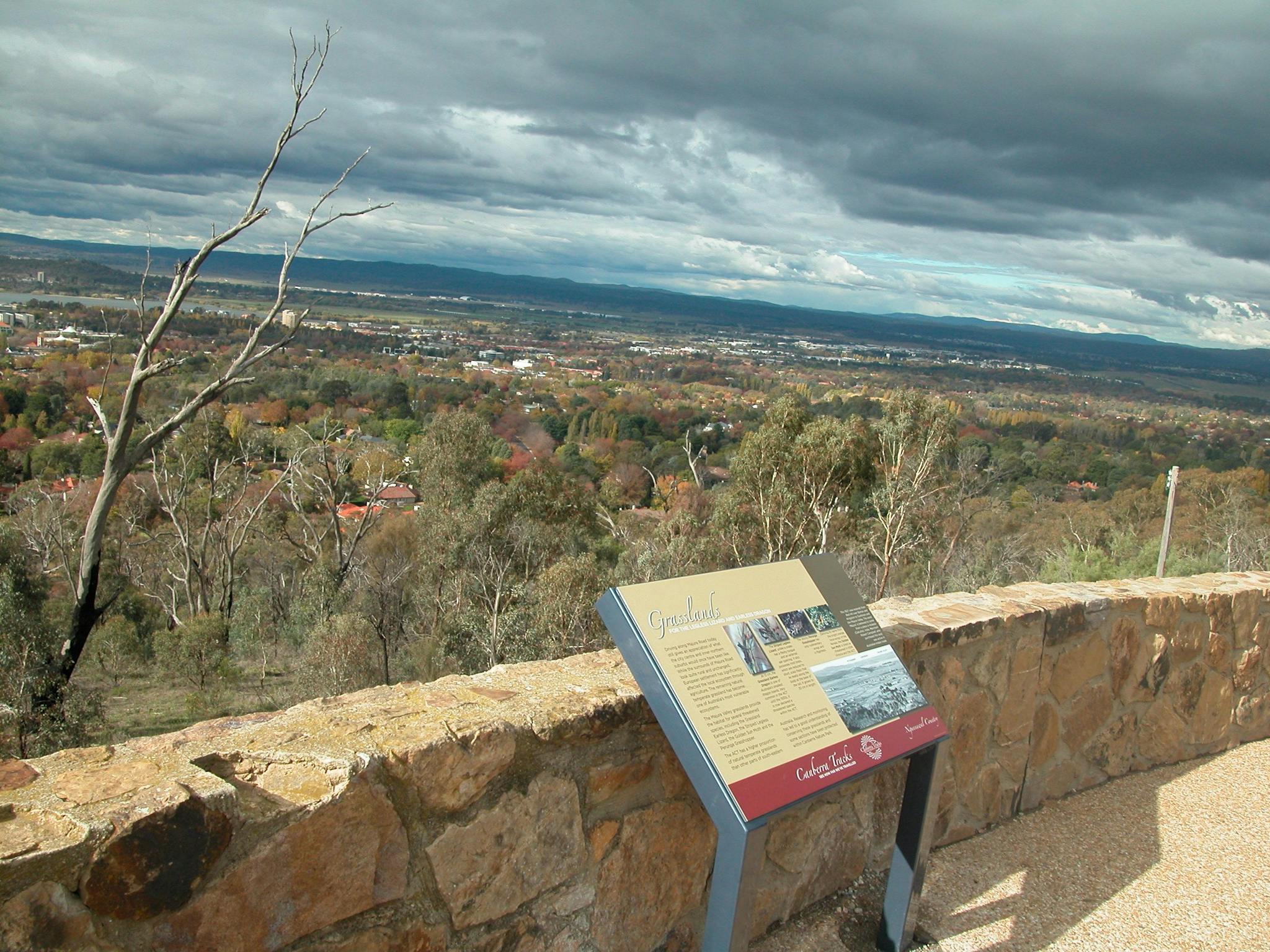 Sign leaning against stone wall with view of trees and distant houses