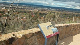 Sign leaning against stone wall with view of trees and distant houses