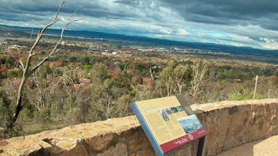 Sign leaning against stone wall with view of trees and distant houses