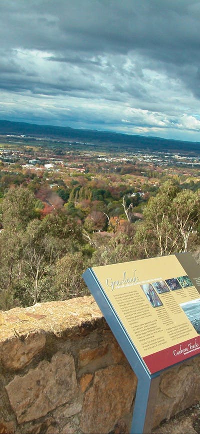Sign leaning against stone wall with view of trees and distant houses