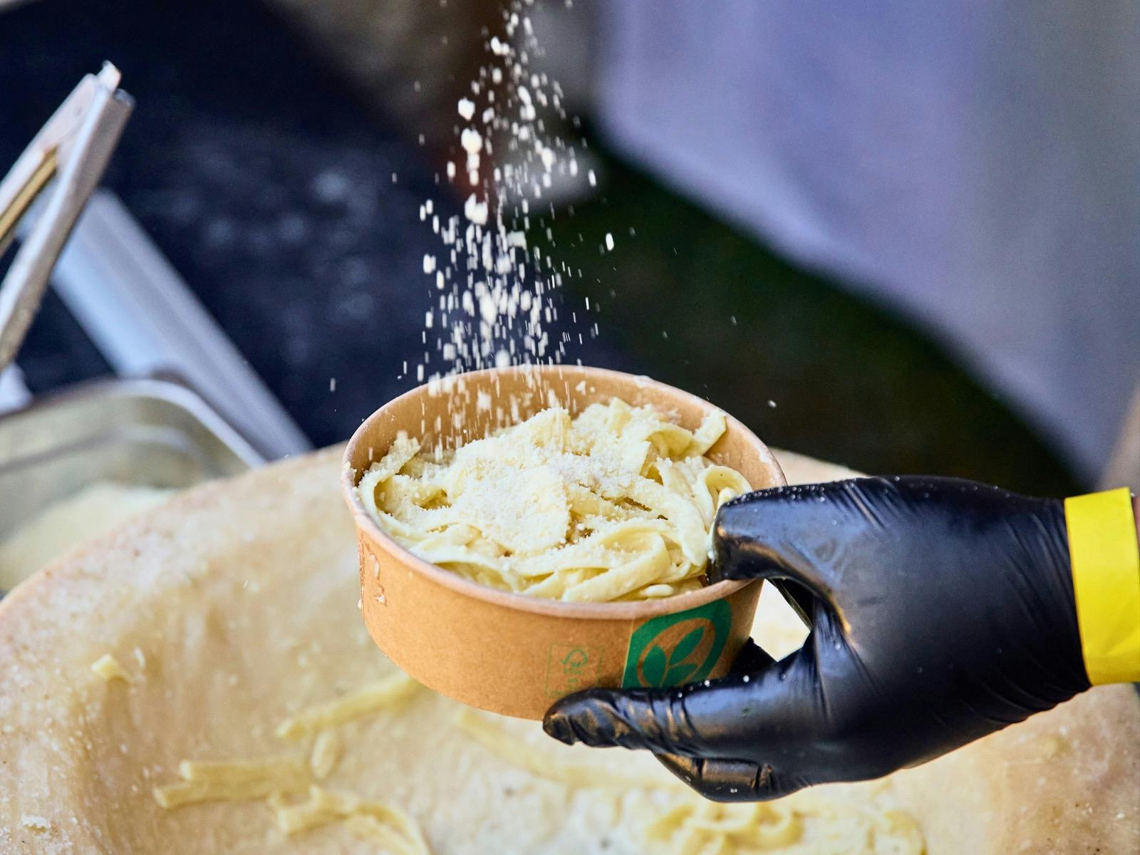 A hand holding a bowl of cacio e Pepe while parmesan is sprinkled in it