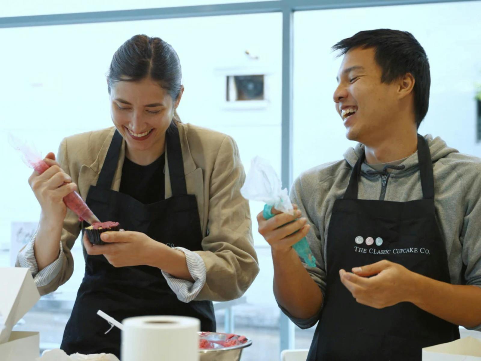 A woman and a man putting frosting in a cupcake during baking classes