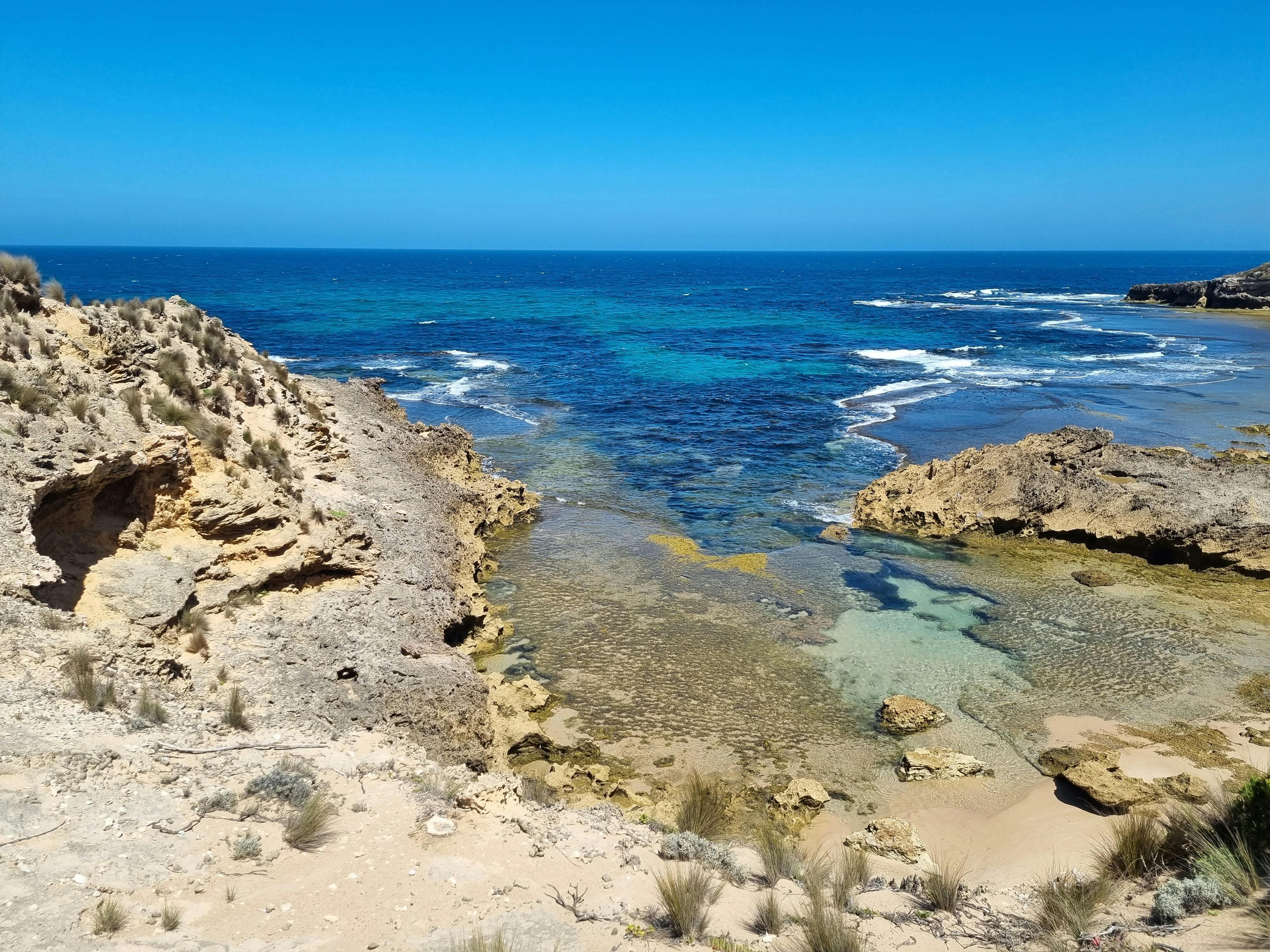 The Bass Strait coastline merges with the blue sky and brown  rocky cliffs.