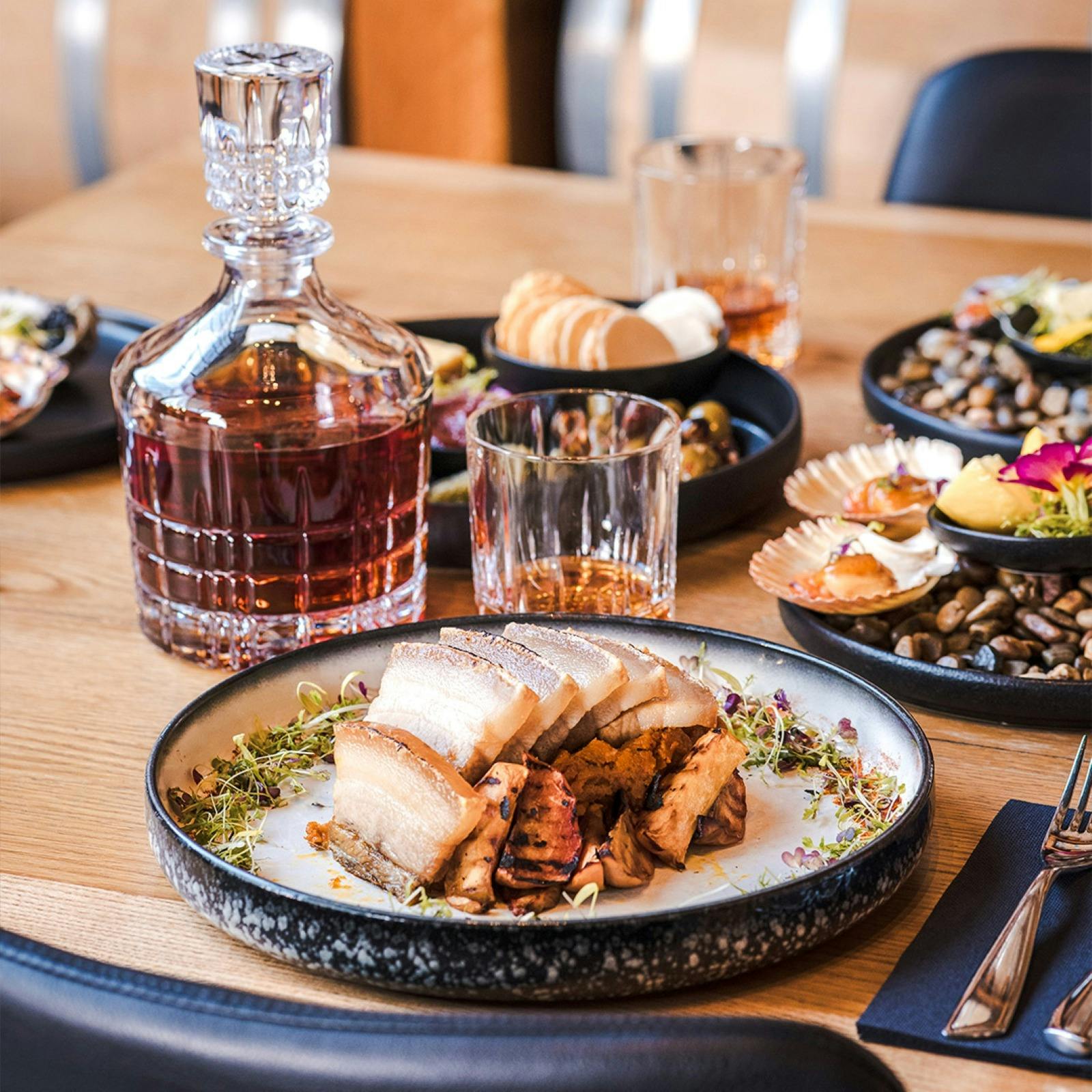 Several plates of colourful food on a table with a crystal bottle and glass of whisky