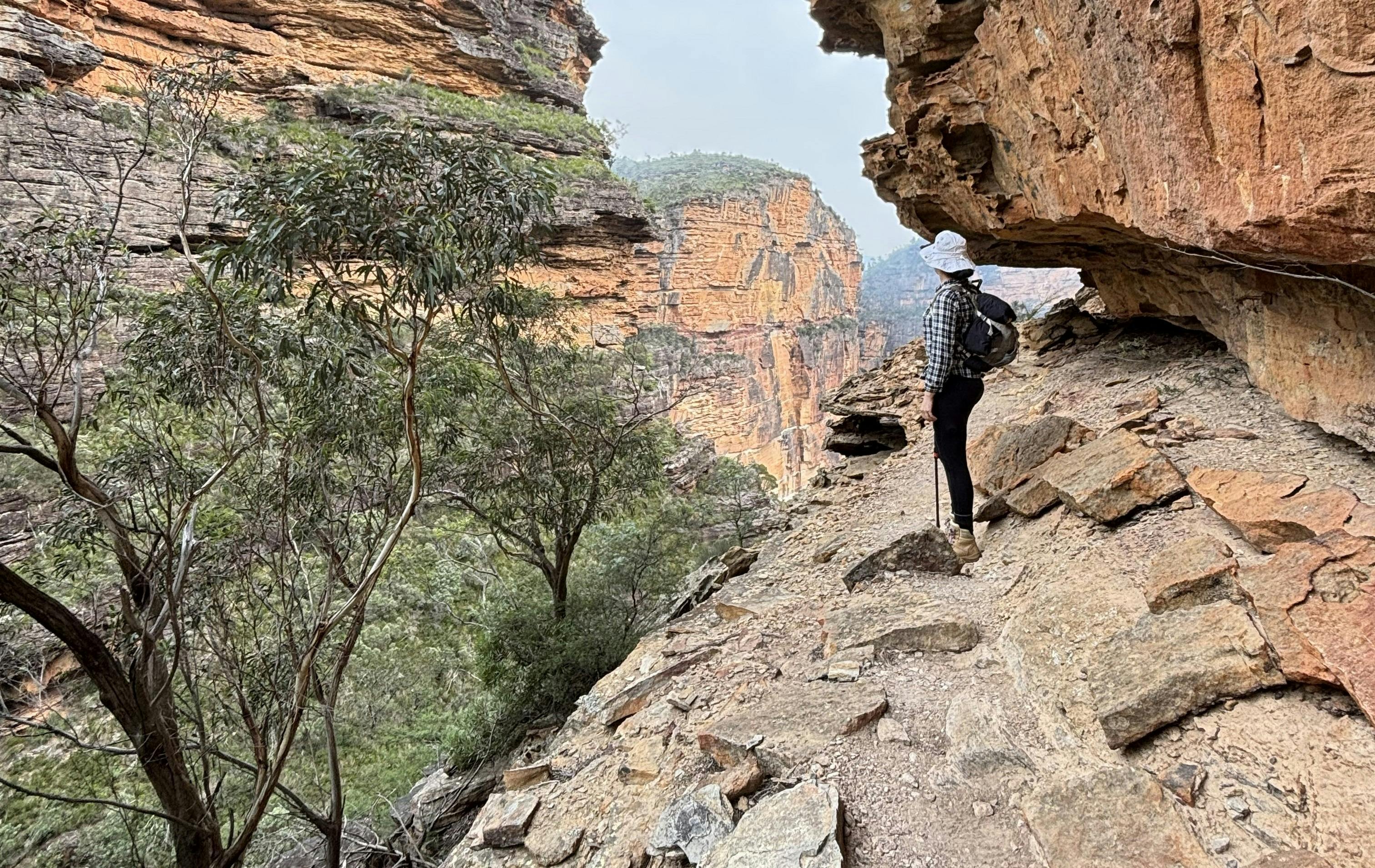 A woman wearing a white hate and checkered shirt standing on the edge of a sandstone gorge.