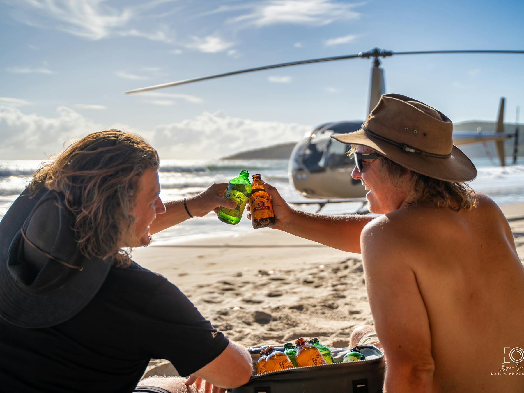 Two Mates enjoying a Brew on a remote beach with the RaptAir Helicopter on the high water mark