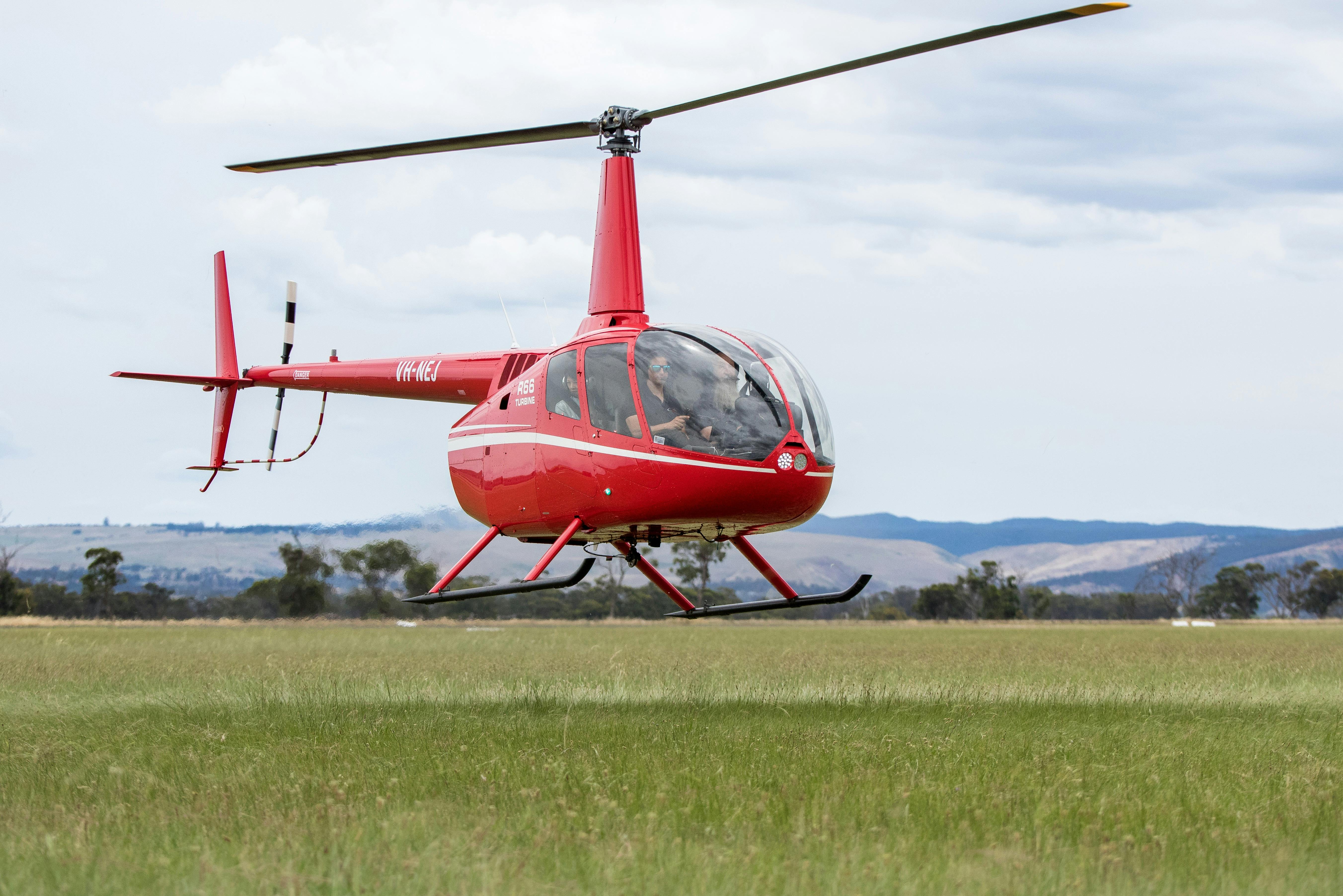 Red helicopter flying over grassy field
