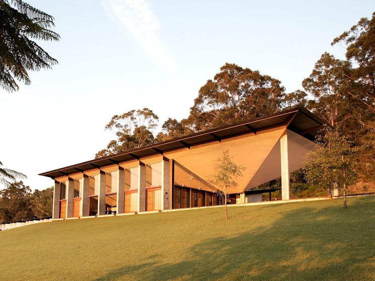 A concrete and wooden concert hall situated at the crest of a hill, surrounded by bush