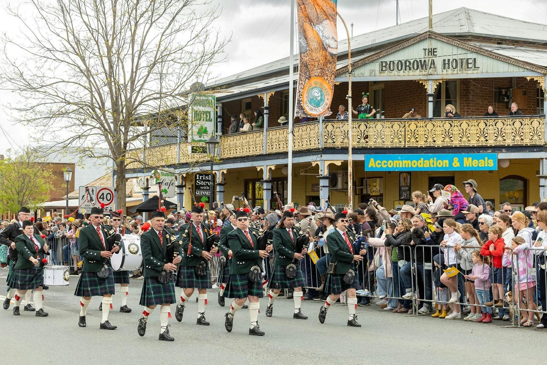 Massed band marching in street parade with crowd watching in front of Irish pub
