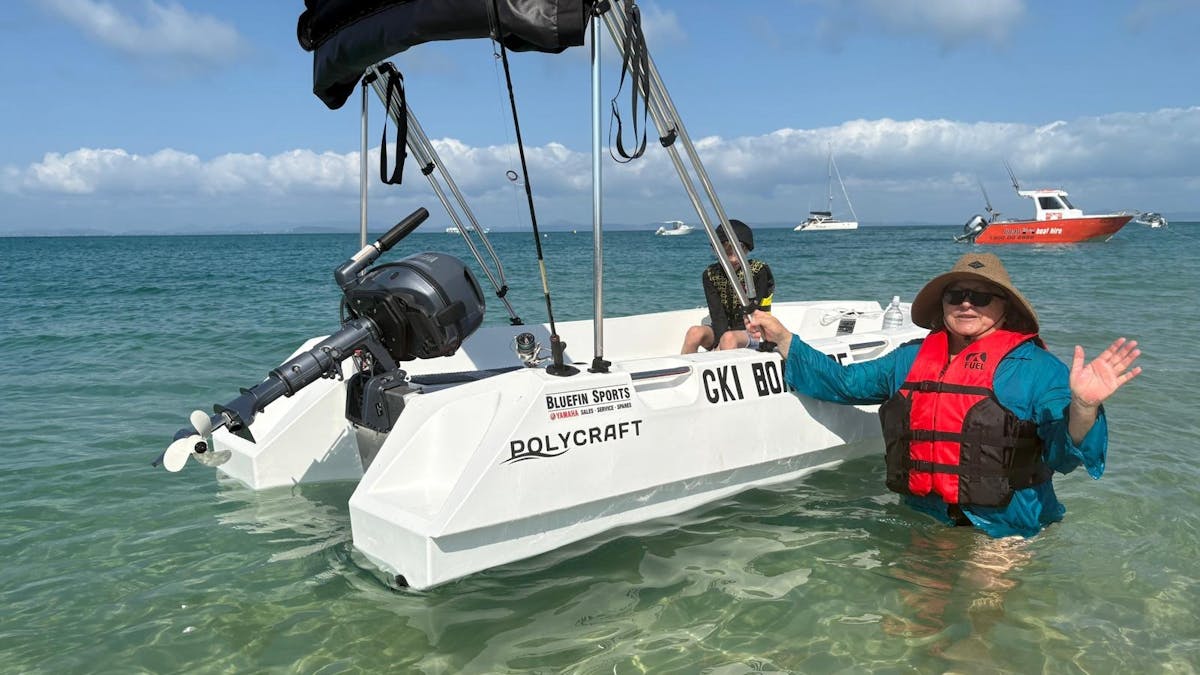 Woman standing beside a white Polycraft hire boat in shallow water at GKI.