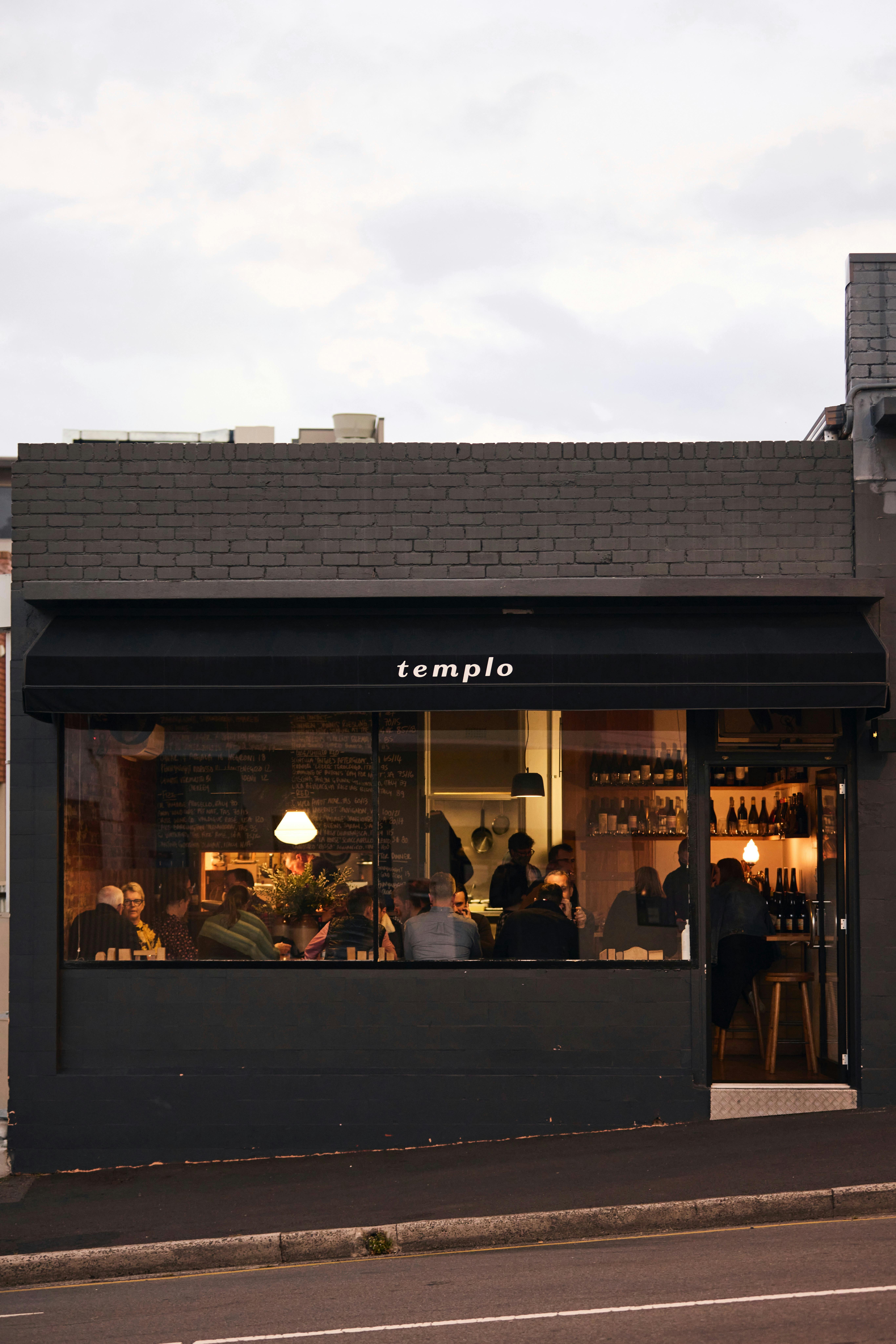 A dark, 20 seat restaurant shot from across the street with a golden glow and bustling with people