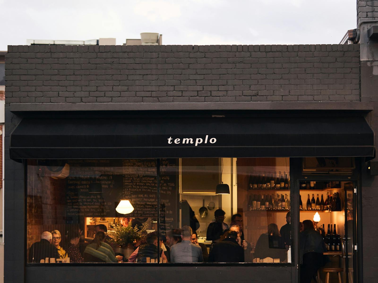 A dark, 20 seat restaurant shot from across the street with a golden glow and bustling with people