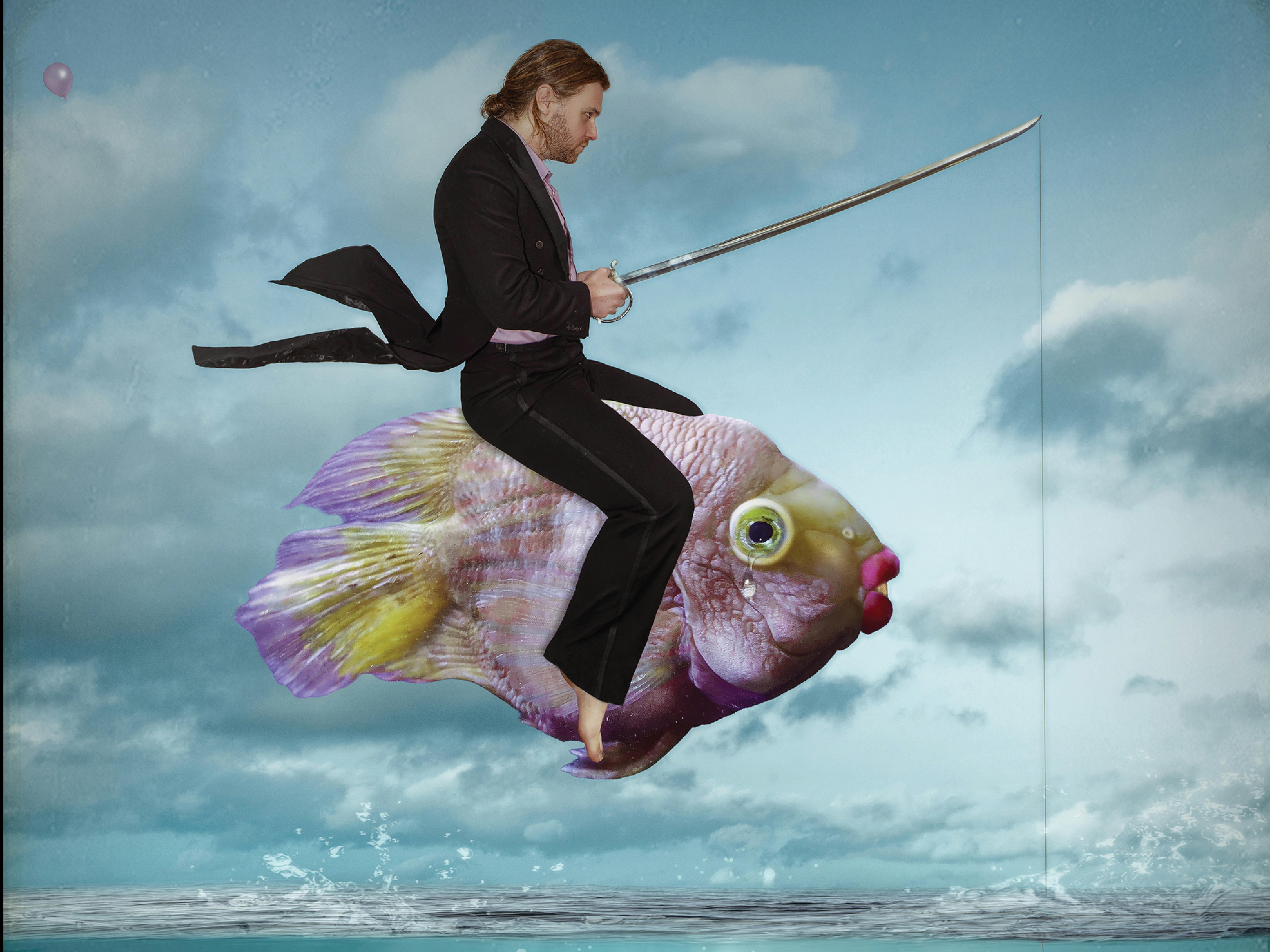 A man wearing a black suit riding a fish through the cloudy sky
