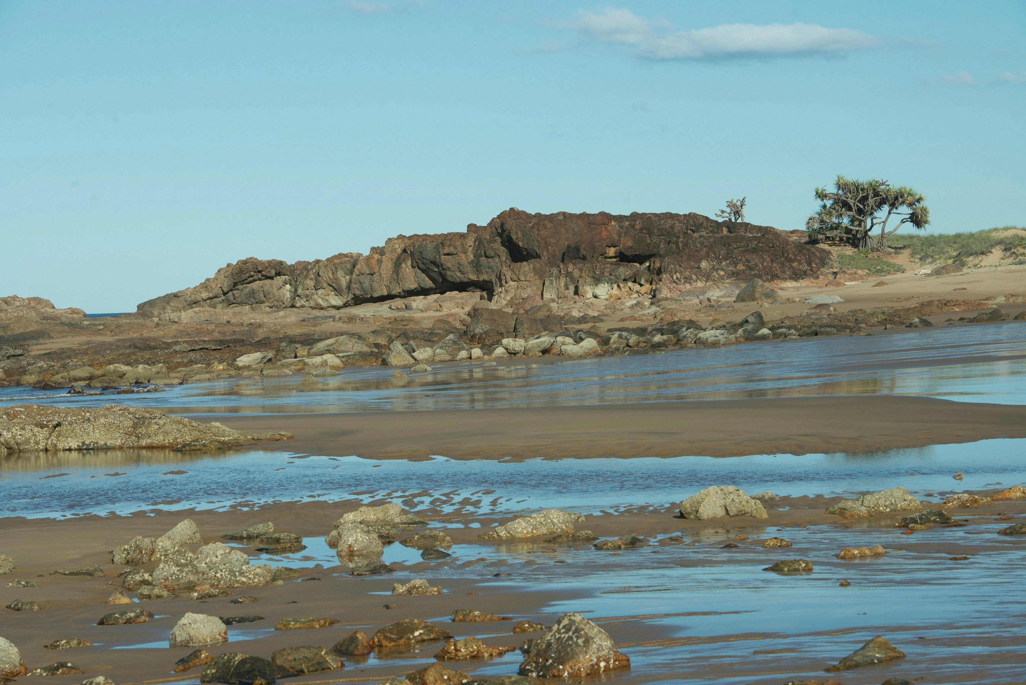 Two people on Wreck Rock Beach walking among  volcanic rock pools , Deepwater National Park