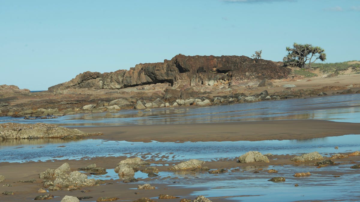 Two people on Wreck Rock Beach walking among  volcanic rock pools , Deepwater National Park