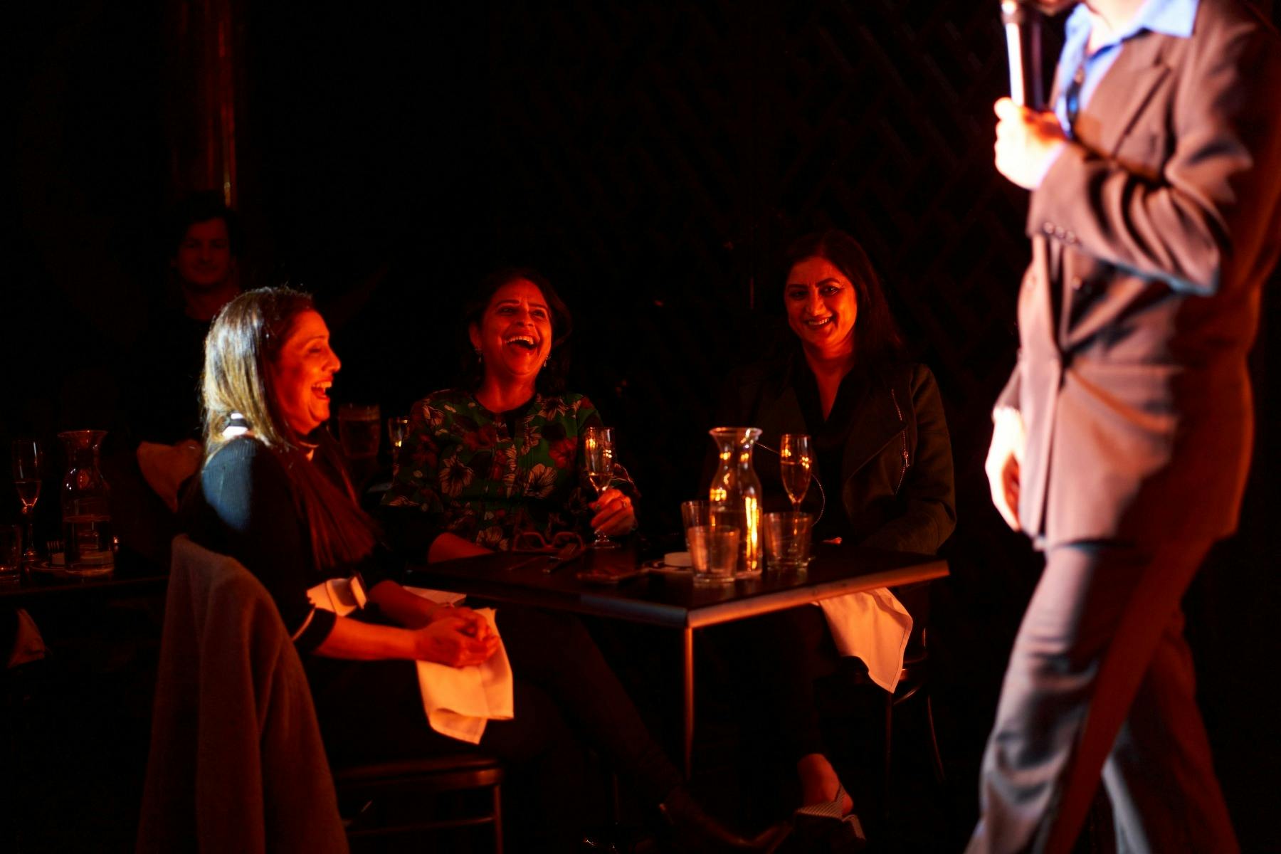 MC stands on the stage from side angle with a microphone while the lit up face of the crowd are la