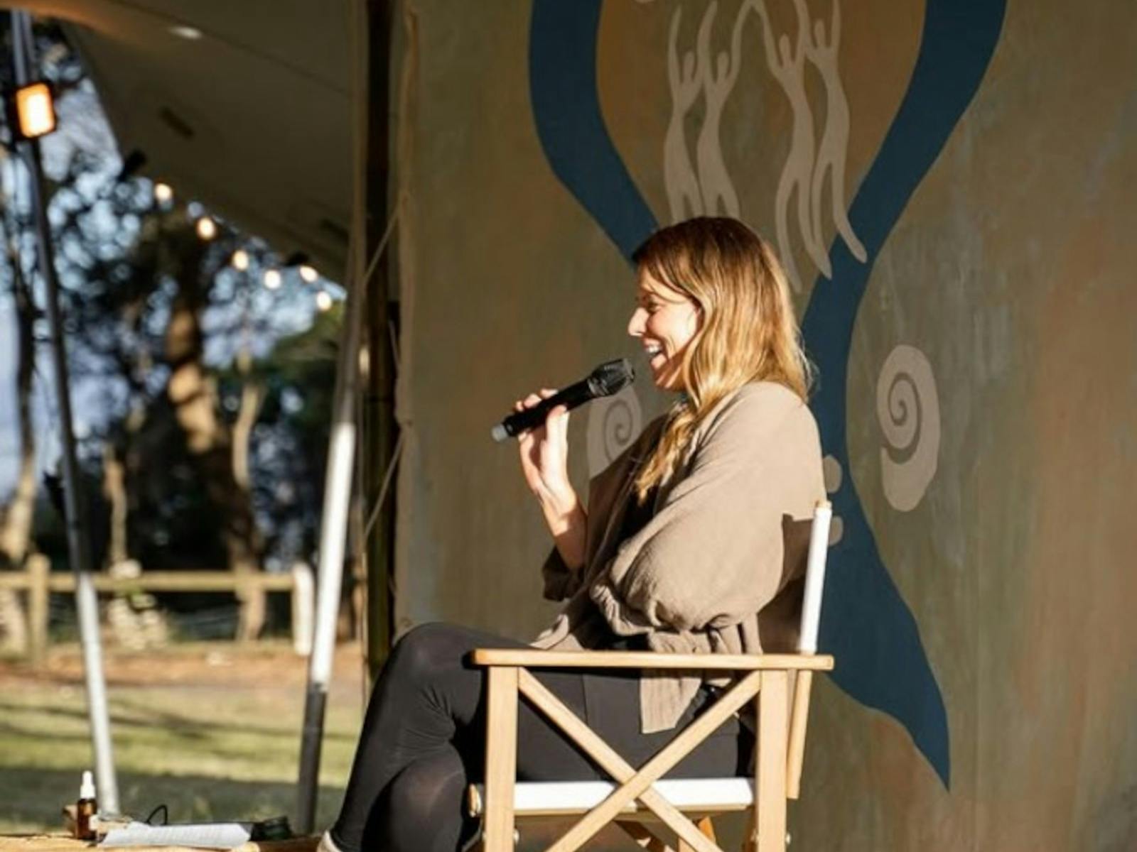 A woman speaking into a microphone on camp chair