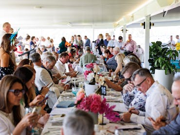 People sitting at long lunch tables decorated with florals. People sitting at long lunch tables decorated with florals.