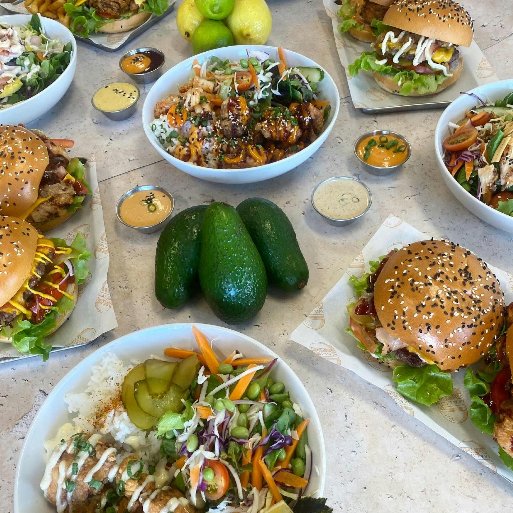 Tablescape of fresh salads, burgers, avocadoes and sauces
